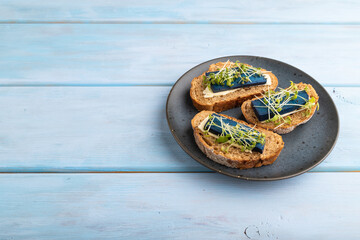 Bread sandwiches with blue lavender cheese and mustard microgreen on blue, side view, copy space.