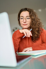 Young woman student using laptop elearning, remote working at home office looking at computer watching webinar, virtual learning, having video conference call hybrid meeting, writing notes. Vertical