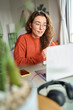 Young woman, female student or worker using laptop elearning or remote working at home office looking at computer watching webinar or having virtual meeting communicating by video call. Vertical.