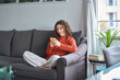 © insta_photos - Young woman sitting on couch holding smartphone, looking at cellphone using cell phone checking mobile apps, reading messages, doing ecommerce shopping, chatting online, watching videos, playing game.