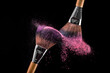 Two make-up cosmetic brushes with pink powder explosion on black background.