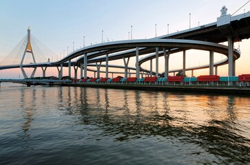 Wall Mural - Sunset scenery of Bhumibol suspension bridge in Bangkok City Thailand, also known as the Industrial Ring Road over Chao Phraya River, with beautiful reflections of golden glow on smooth water at dusk