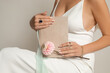 Unrecognizable cropped woman in white dress with decollete holding blank diary notebook and flower in hands in studio