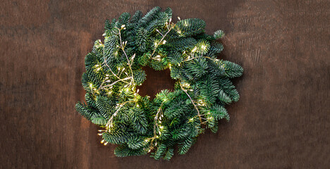 Wall Mural - christmas wreath with golden lights garland on dark wooden background top view, copyspace. xmas, nat