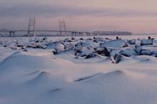 Cable-stayed Bridge Over The River In Winter At Sunset. St. Petersburg In Winter. Rocks Under The Snow In The Foreground