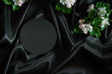 Round Geometric Platform Podium Stand For Cosmetics Product Presentation And Spring Blooming Tree Branches With White Flowers On Elegant Black Silk Satin Fabric Background. Top View