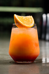 Poster - Alcoholic cocktail Tequila Sunrise made from tequila, orange juice, grenadine or pomegranate syrup and ice, garnished with an orange slice on a bar.