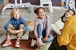 © Seventyfour - Group of cute little learners of nursery school sitting on the floor of classroom while listening to teacher reading them book