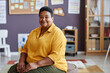 © Seventyfour - Portrait of experienced African American female teacher or coach in yellow shirt sitting in front of camera in classroom of nursery school