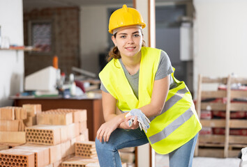 Positive smiling young female design architect in helmet standing at indoor building site