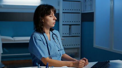 Physician nurse standing at desk table late at night in hospital office typing medical report during appointment. Assistant checking patient disease symptoms planning health care treatment