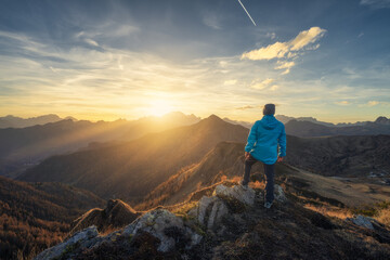 Wall Mural - Man on stone on the hill and beautiful mountains in haze at colorful sunset in autumn. Dolomites, Italy. Sporty guy, mountain ridges in fog, orange grass and trees, blue sky with sun in fall. Hiking	