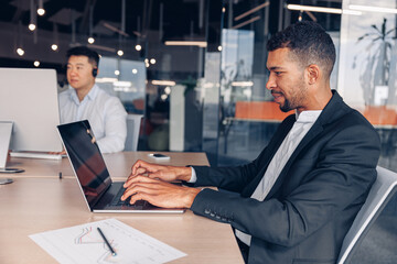 Handsome african businessman working laptop while sitting in modern office on colleague background