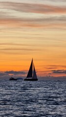 Poster - Scenic vertical view of a sailboat in a tranquil sea during a mesmerizing sunset