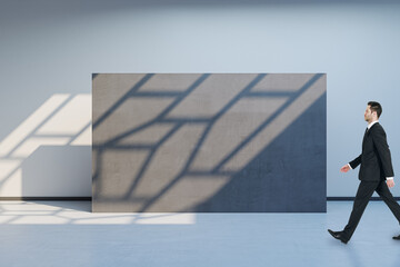 Canvas Print - Side view of blurry man walking in spacious gallery interior with empty poster and sunlight shadow on concrete wall. Mock up.