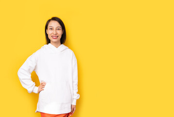 Smiling Asian woman in white hoodie looking at camera and smiling. Chinese woman looking at camera Clothes empty space for your information copy space, yellow background