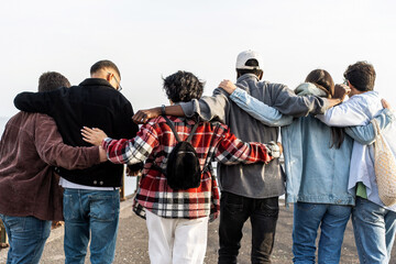 Unite group of multiethnic young friends walking outdoors - cheerful men and women hugging together