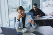 © Дмитрий Ткачук - A female manager sits at a desk using a laptop in a modern office with a colleague in the background. Working atmosphere in an office with large windows.