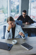 © Дмитрий Ткачук - A female manager sits at a desk using a laptop in a modern office with a colleague in the background. Working atmosphere in an office with large windows.