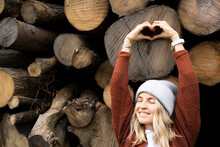 Smiling Woman Making Heart Shape In Front Of Logs