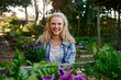 © StratfordProductions - Young caucasian woman wearing checked shirt looking at camera by flowers in plant nursery