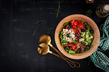 Fresh salad with avocado, tomatoes, mozzarella cheese, sweet peppers and black olives on wooden bowl. Top view, above