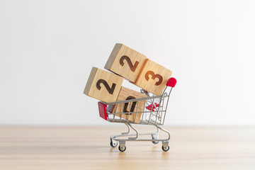 Happy new year with 2023 block in shopping trolley cart on table. E commerce, online shopping, finance, consumer economy and celebration concepts