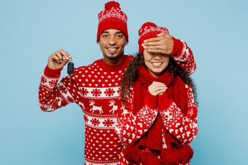 Merry young couple two man woman wear red Christmas sweater Santa hat posing cover eyes give car keys keyless system isolated on plain pastel light blue background Happy New Year 2023 holiday concept