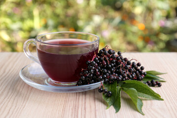 Glass cup of tasty elderberry tea and Sambucus berries on wooden table outdoors