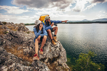 hikers with backpacks sitting on cliff enjoying at the mountain lake