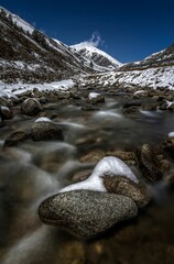 Canvas Print - Beautiful shot of rocky stream in middle of snow covered valley at foot of Dongda Mountains, Tibet