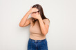 Young caucasian cute woman isolated on white background blink at the camera through fingers, embarrassed covering face.