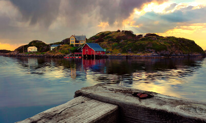 sunset with storm and clouds in the arctic sea. Houses on an island with green vegetation