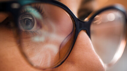 Businesswoman working at night looking at monitor, reflections in eyeglasses. Work online late screen computer reflection on glasses. Using internet, watching, studying web