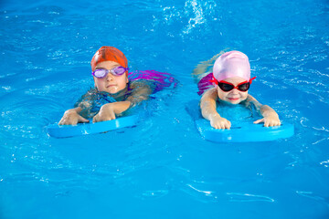 Wall Mural - Two little girls having fun in pool learning how to swim using flutter boards