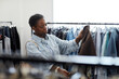 Waist up portrait of black young woman looking at clothes in thrift store