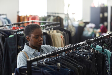 Wall Mural - High angle portrait of black young woman looking at clothes on racks in thrift store