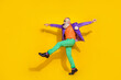 © deagreez - Full length photo of positive funky man wear purple velvet jacket walking hands sides discotheque isolated yellow color background