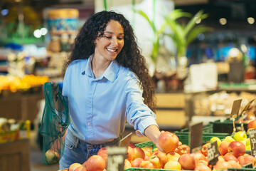 Happy woman buyer in supermarket, Latin American woman buys apples, fruits and vegetables, puts in an ecological bag.