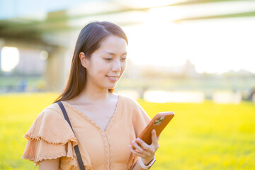 Poster - Asian woman use of smart phone at park under sunlight flare