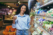 © Liubomir - Portrait of a beautiful vegetarian woman in a supermarket, a Hispanic woman smiling and looking at the camera and smiling chooses broccoli vegetables in a grocery store.