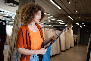 Young smiling woman holding fabric samples in blurred textile shop