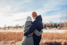 Back View Of Loving Couple Walking By Winter River. Man And Woman Hugging Enjoying Snowy Landscape Outdoors
