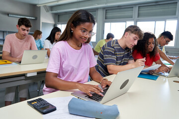 Portrait focus on the first female student using laptop, concentrated with cheerful face in classroom. Group of multiethnic colleagues in class, back to school. Technological education arrived.