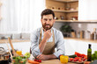 Smiling attractive adult european bearded man chef in apron look at camera in minimal kitchen interior