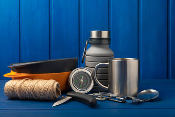 Set of tourist equipment on a blue texture background. EDC set. Flat layout. Camping plate, mug, bottle, spoon and compass.