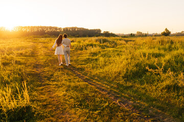 Wall Mural - wide shot of unrecognizable happy young couple in love embracing walking in beautiful green filed to