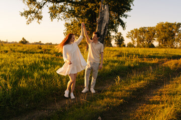 Wall Mural - happy young couple in love dancing together on green meadow in summer evening during sunset with sof