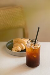 Poster - Vertical shot of a glass of iced coffee with a croissant