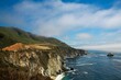 Big Sur's rugged landscape of sea waves crashing the cliffs under a cloudy sky, California